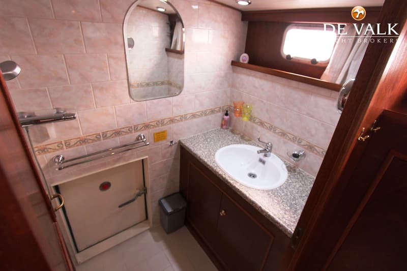 Een badkamer met een wastafel, spiegel, douchekop, handdoekrekken, een patrijspoort en een luik in de muur.