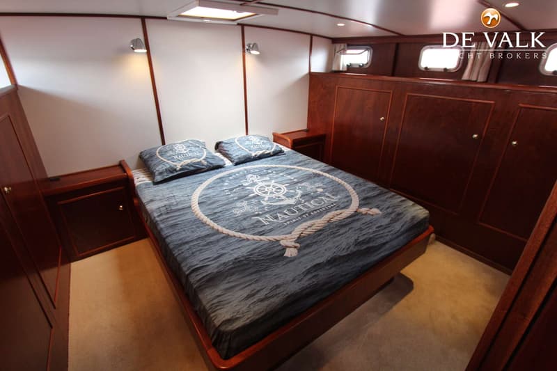 Een slaapkamer met een tweepersoonsbed met nautisch beddengoed, houten kasten en witte wanden.