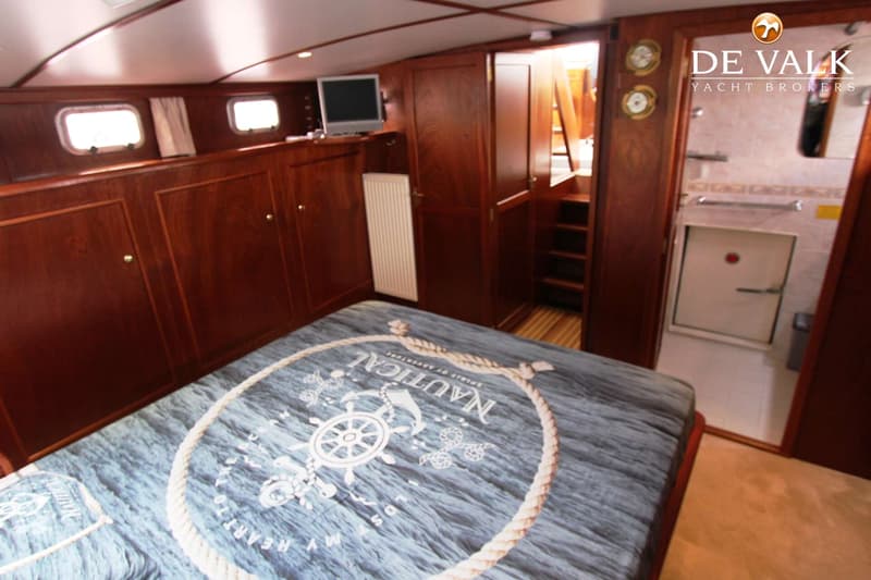 Een slaapkamer in een boot met een bed, houten kasten, patrijspoorten, een televisie en een badkamer.