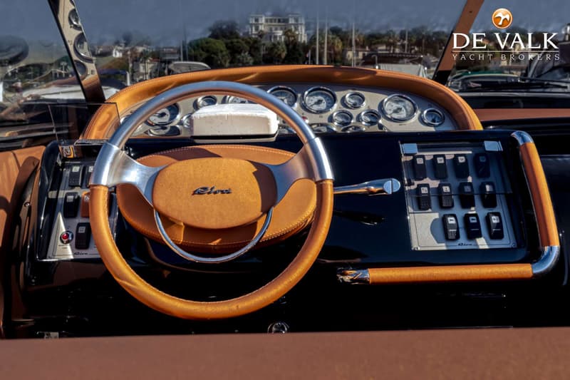 Een close-up van een stuur met bruin leer en zilverkleurige accenten, met daarachter een dashboard met meters en schakelaars.