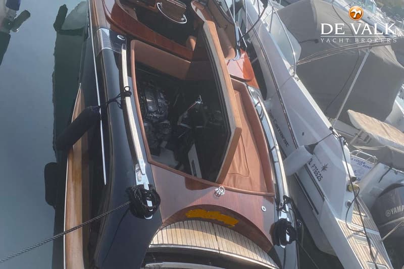Een donkerblauwe boot met houten details en een open kuip ligt aangemeerd naast andere boten. — Riva Aquariva Cento