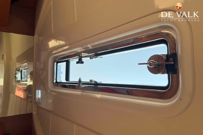 Een rechthoekig patrijspoort met een metalen frame en sluitingen is zichtbaar in een lichte wand.