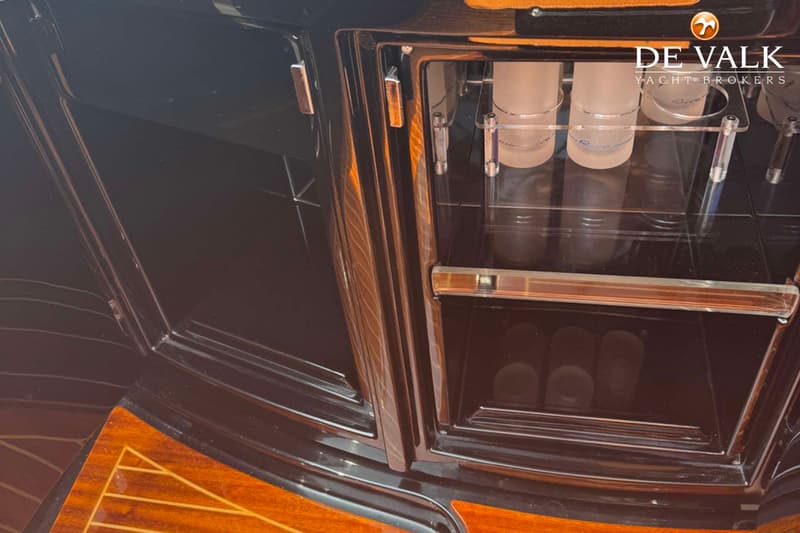 Een detailfoto van een donkerbruine houten kast met een glazen vitrine waarin glazen staan.