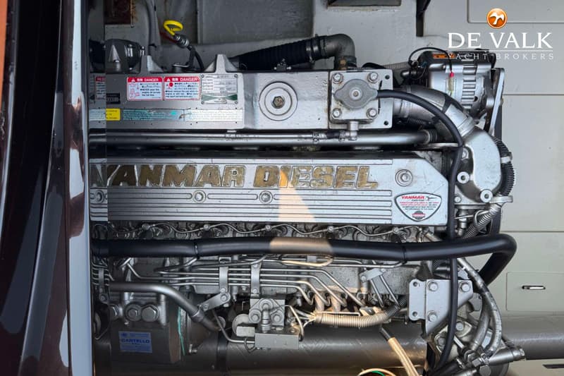 Een close-up van een Yanmar dieselmotor met diverse leidingen en waarschuwingsstickers.
