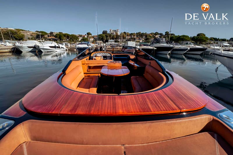 Een luxe motorboot met houten dek en oranje lederen bekleding ligt in een haven vol met andere boten. — Riva Aquariva Cento