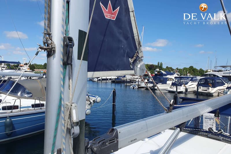 Een blauw zeil met een rood kroonlogo en de tekst "ELVSTRÖM SAILS" is zichtbaar, met een mast en giek.