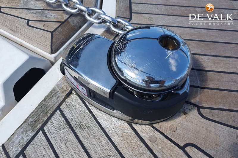 Een chromen ankerlier met de tekst "Quick" erop, verbonden met een ankerketting, op een houten dek.