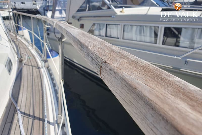 Een close-up van een houten handreling op een boot, met een deel van het dek en een andere boot op de achtergrond.