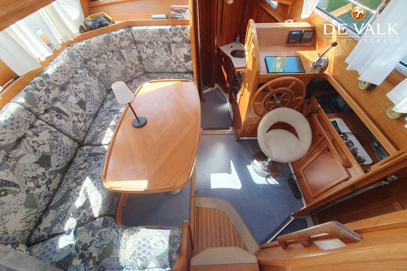 De foto toont het interieur van een boot met een zithoek, tafel, stuurstand en een kleine keuken. — Nauticat 32