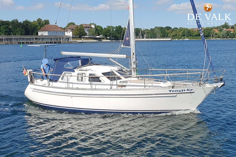 Een witte zeilboot met blauwe strepen en de naam "Tongji-Er" vaart op blauw water. — Nauticat 32