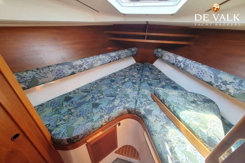 De foto toont een kajuit met een V-vormig bed met blauwgroene kussens, houten wanden en een dakraam. — Nauticat 32