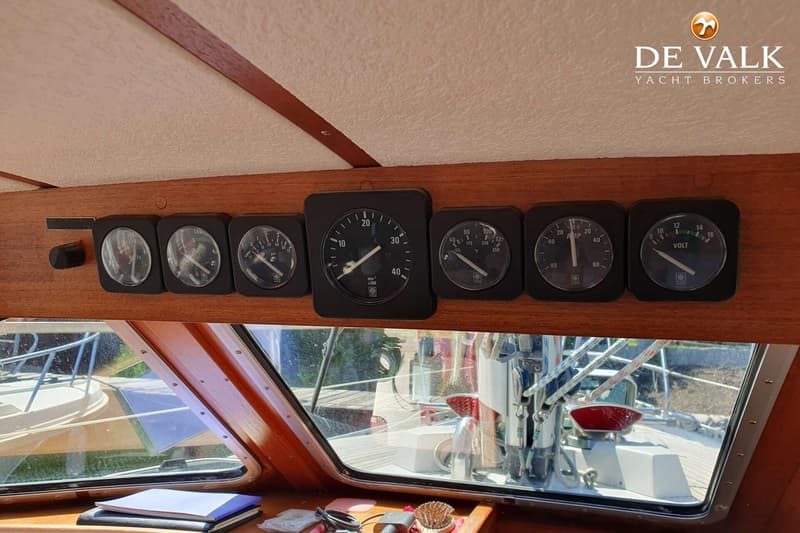 Zeven zwarte, ronde meters zijn gemonteerd op een houten paneel boven een raam in een boot. — Nauticat 32