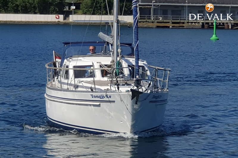 Een witte zeilboot met de naam "Tongji-Er" vaart op blauw water, met een man aan het roer en een groen boei in de verte.