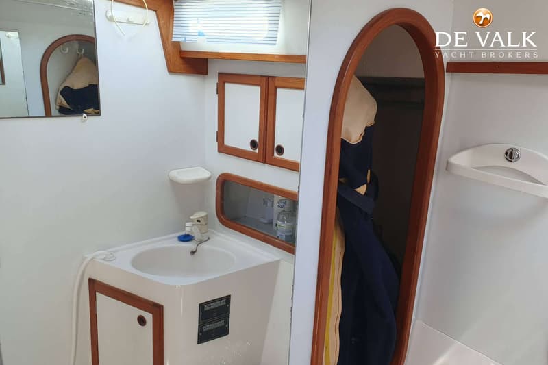 Een interieurfoto van een boot met een wasbak, spiegel, kastjes en een doorgang naar een andere ruimte. — Nauticat 32