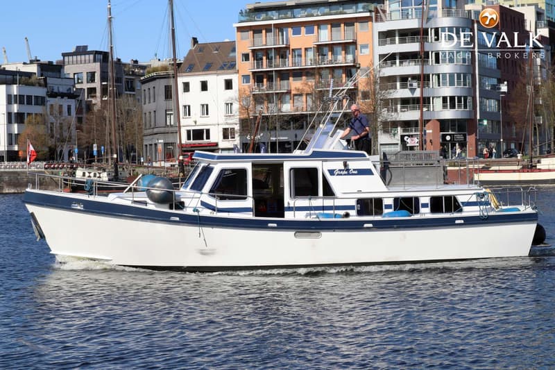 Een witte motorboot met blauwe accenten en de naam "Grape One" vaart op het water, met een man aan het roer.