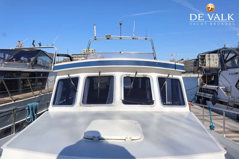 De foto toont de voorkant van een witte boot met blauwe accenten, met ramen en een luik op het dek. — TMBoats TMB36eco