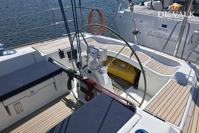 De foto toont de kuip van een zeilboot met een stuurwiel, blauwe kussens en een houten dek. — Beneteau First 47.7
