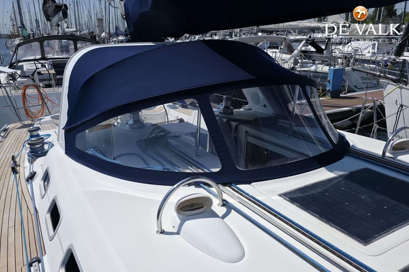 Een deel van het dek van een zeilboot met een donkerblauwe buiskap, touwen, een zonnepaneel en een luik.