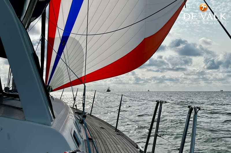 Een zeilboot met een wit, rood en blauw zeil vaart op zee onder een bewolkte hemel. — Beneteau First 47.7
