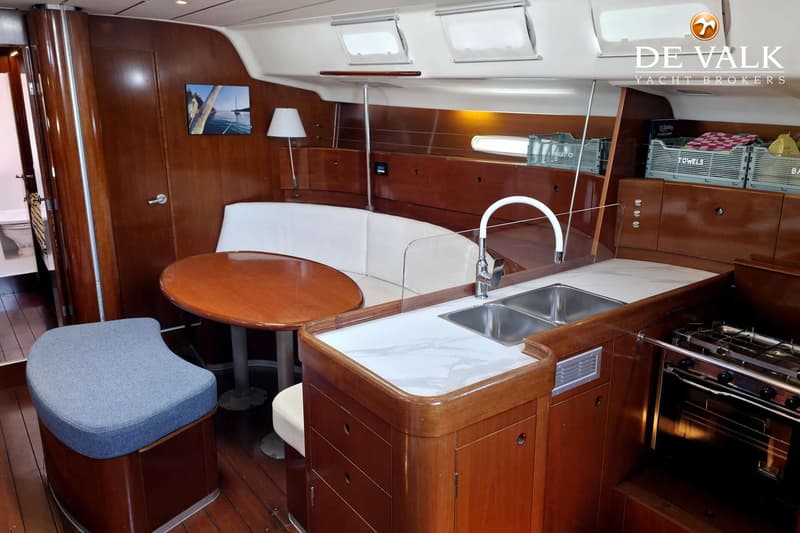 De foto toont het interieur van een boot met een kombuis, zithoek en houten afwerking. — Beneteau First 47.7