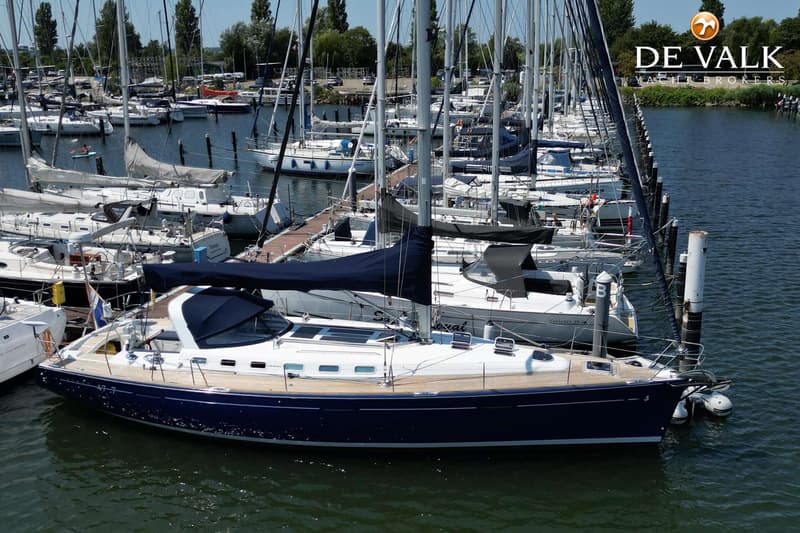 Een donkerblauwe zeilboot met een houten dek en een donkerblauwe huik ligt aangemeerd in een jachthaven.
