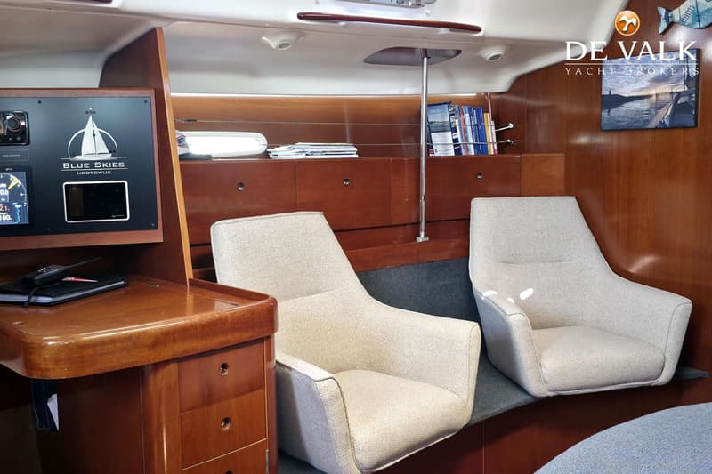 De foto toont het interieur van een boot met twee lichte fauteuils, een houten bureau met lades en een navigatiepaneel.