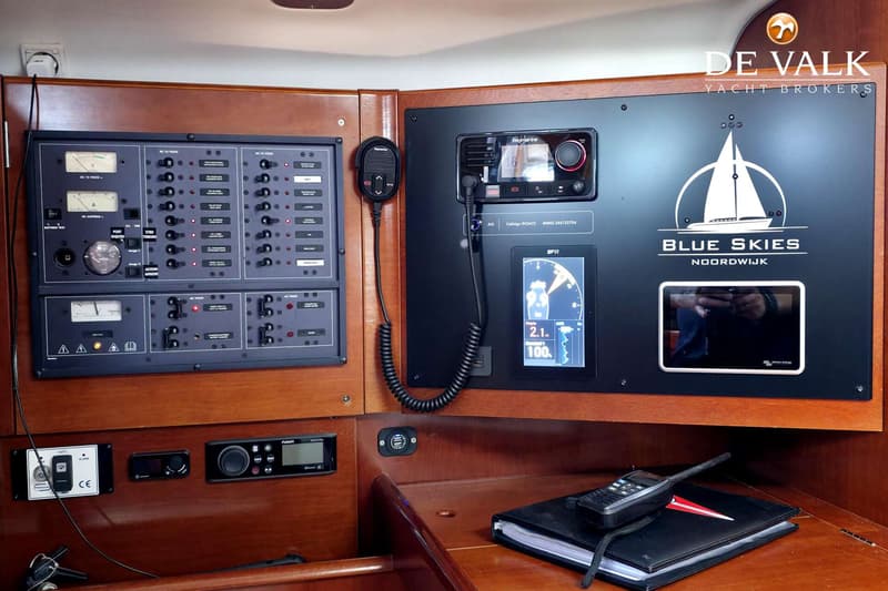 Een houten paneel met diverse navigatie-instrumenten, schakelaars en meters, inclusief een Raymarine marifoon en een scherm…