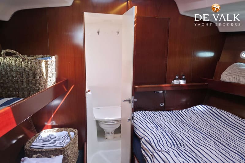 Een interieur van een boot met een bed met blauw-wit gestreept dekbed, een toiletruimte en houten wanden.