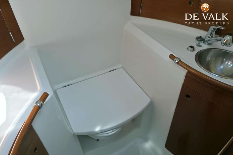 Een witte toiletruimte met een toilet met gesloten deksel, een metalen wasbak en een kraan.