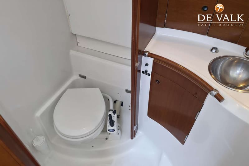 De foto toont een boottoilet met een Jabsco pomp, een toiletborstel en een wastafel met een metalen kom.