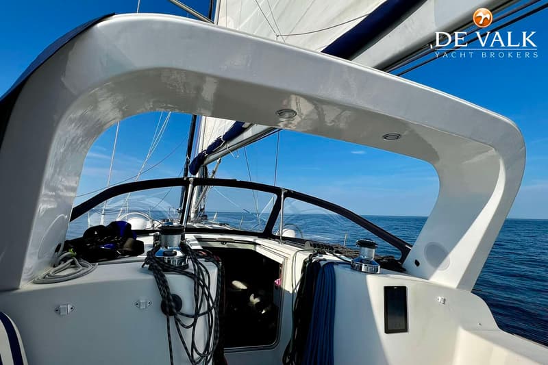 Een witte zeilboot vaart op open water onder een helderblauwe lucht, met zeilen gehesen en touwen opgerold.