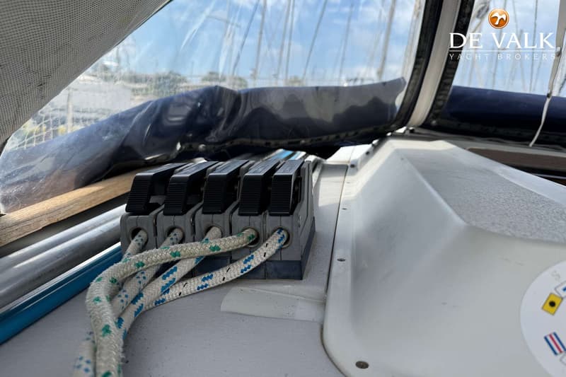 De foto toont een detail van het dek van een boot met vier touwklemmen en touwen, met een doorzichtig zeil op de achtergrond.