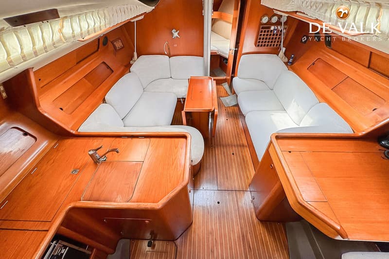 De foto toont het interieur van een boot met houten vloer en wanden, witte banken en een tafel in het midden.