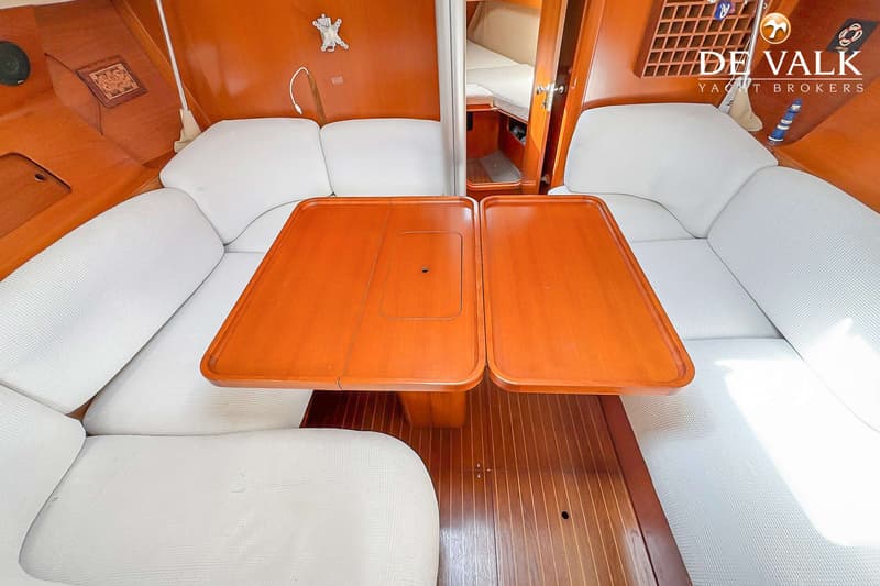 Een interieur van een boot met een houten vloer, twee houten tafels en witte banken aan weerszijden. — Grand Soleil 38