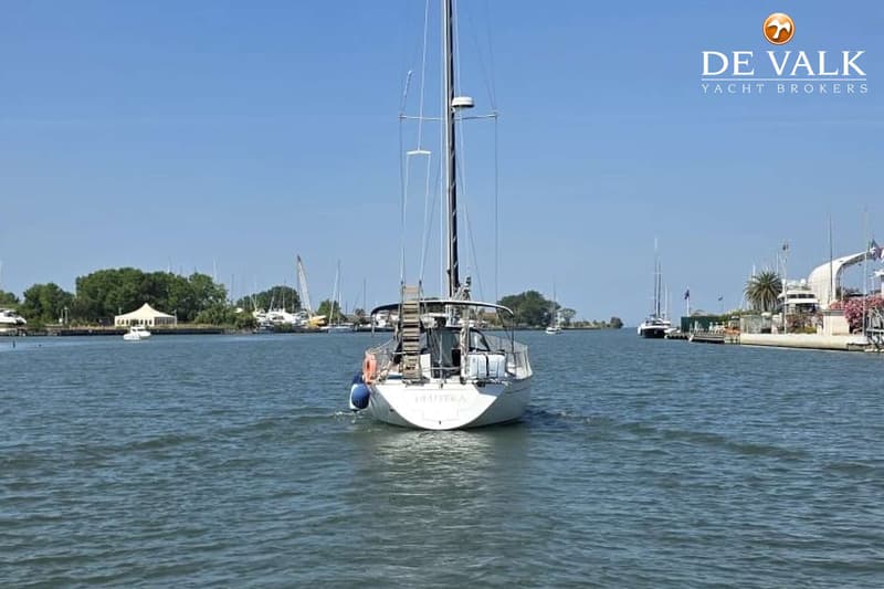 Een witte zeilboot met de naam "DEUTERA" op de spiegel vaart op rustig water onder een helderblauwe lucht. — Grand Soleil 38