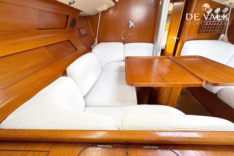 Een kajuit met houten wanden en een U-vormige witte bank rondom een houten tafel. — Grand Soleil 38