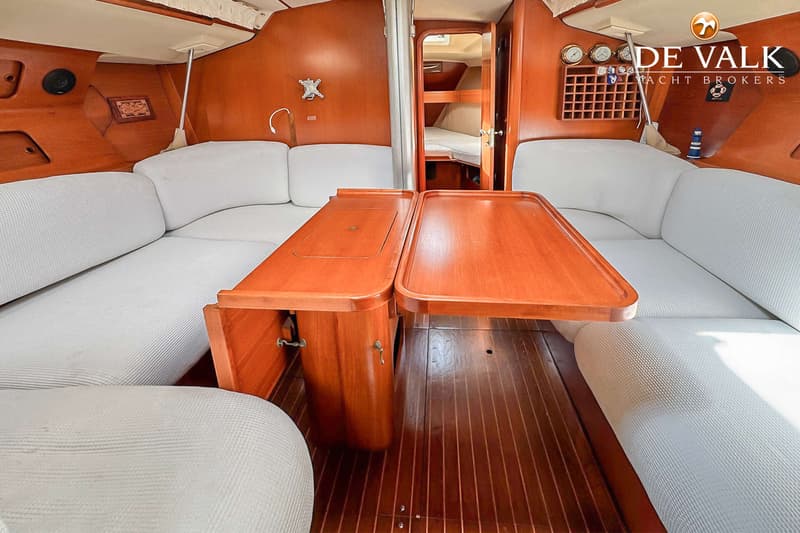 Een interieur van een boot met houten wanden en vloer, witte banken en een houten tafel in het midden. — Grand Soleil 38