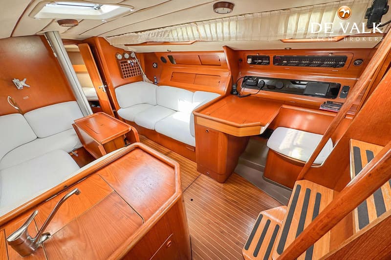 Een interieur van een boot met houten afwerking, witte banken, een kombuis en een navigatiehoek. — Grand Soleil 38