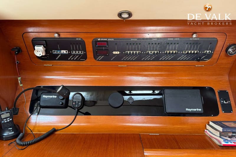 Een houten paneel met diverse schakelaars, meters, een stopcontact en Raymarine apparatuur.