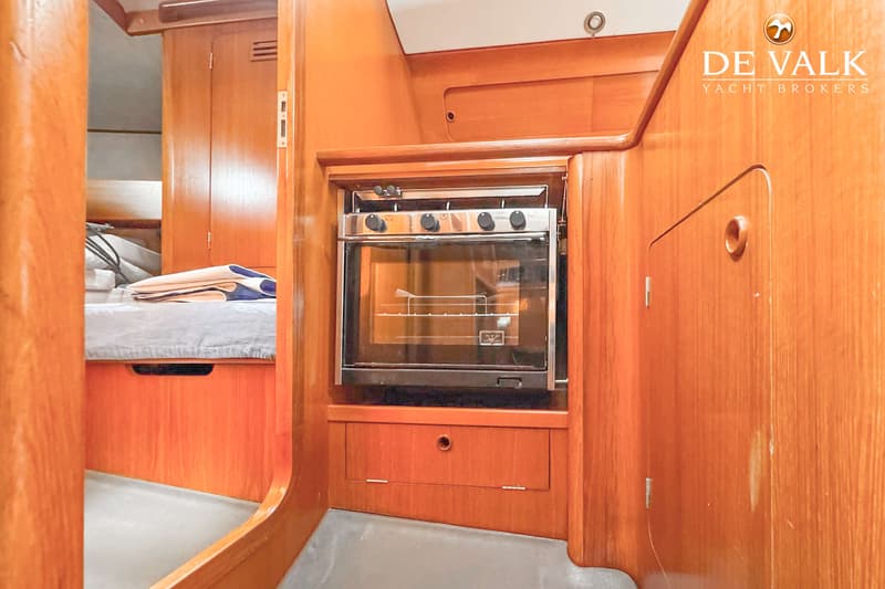 Een interieur van een boot met houten wanden, een fornuis met oven, een bed en het logo "DE VALK YACHT BROKERS".