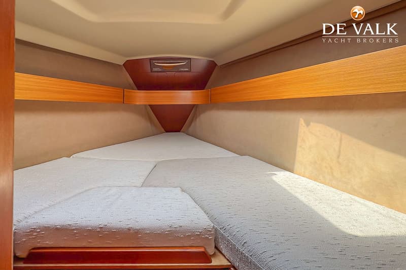 De foto toont een kajuit met een V-vormig bed met witte matrassen en houten accenten. — Grand Soleil 38