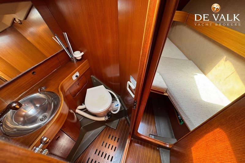 Een interieur van een boot met een toilet, wasbak, houten wanden en vloer, en een bed met witte kussens. — Grand Soleil 38