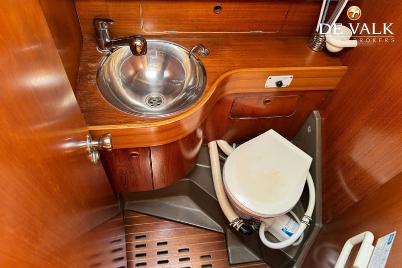 Een badkamer met een metalen wasbak en kraan, een toilet met een witte zitting en houten wanden en vloer.
