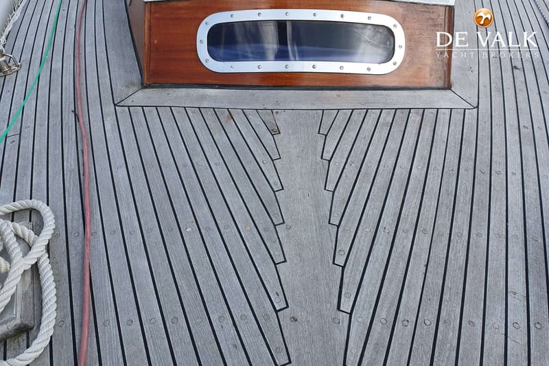 Een houten dek met een kajuitopbouw met een raam en een touw aan bakboord.