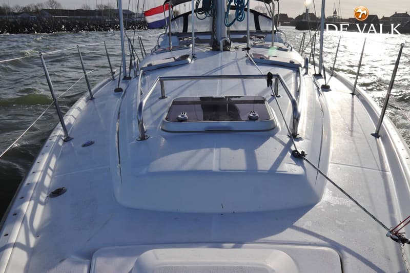 Een wit dek van een zeilboot met een luik, relingen en een Nederlandse vlag op de achtergrond. — Beneteau Oceanis 411