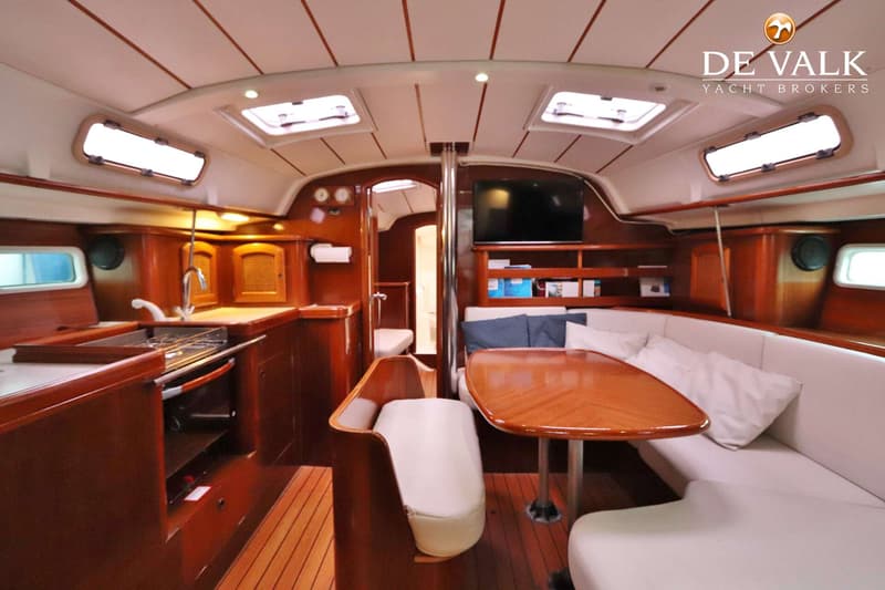De foto toont het interieur van een boot met een kombuis, een zithoek met tafel en een doorgang naar een andere ruimte.