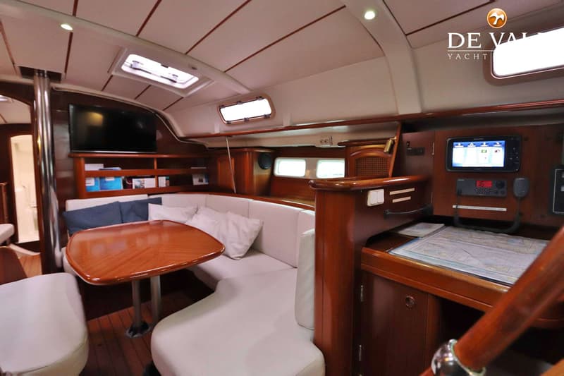 De foto toont het interieur van een boot met een houten tafel, witte banken, een televisie en navigatieapparatuur.