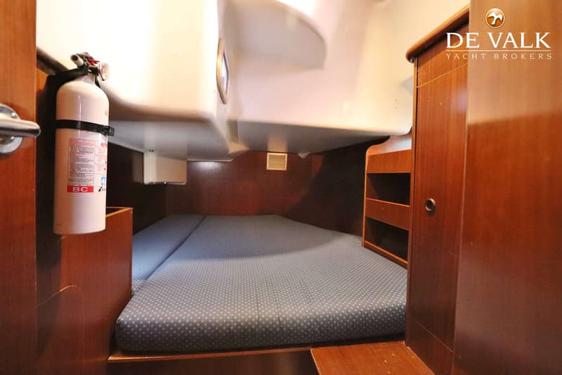 Een kajuit met een tweepersoonsbed met blauw gestippeld matras, houten wanden en een brandblusser. — Beneteau Oceanis 411