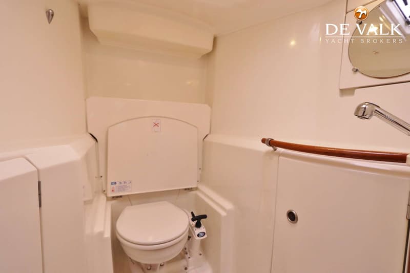 Een witte scheepstoiletruimte met een toilet, een kraan en een houten handgreep.