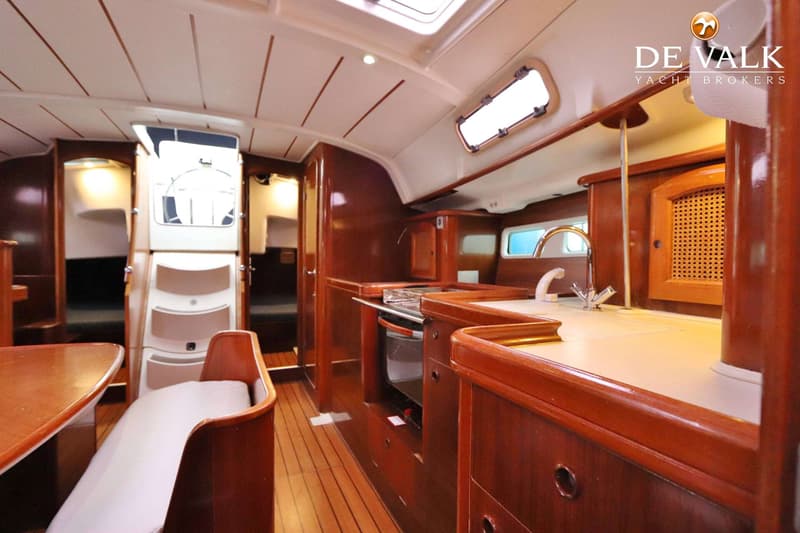 Een interieur van een boot met houten vloer en meubilair, een kombuis met gootsteen en kookplaat, en een trap naar de kuip.
